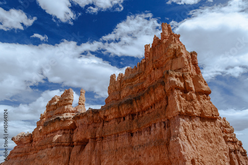 Giant Hoodoo towers skyward in Bryce Canyon National Park, Utah, against a background of white clouds and deep blue sky.