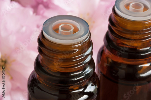 Two bottles of essential oil with pink blossoms in the background