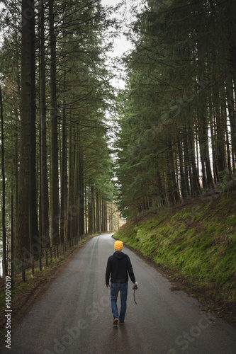 Man walking away down road between trees with camera © Fergus Coyle