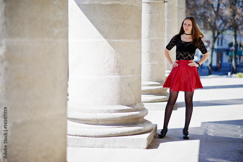 Portrait of girl with black choker necklace on her neck and red leather skirt against stone columns. Portrait of girl with black choker necklace on her neck and red leather skirt against stone columns.