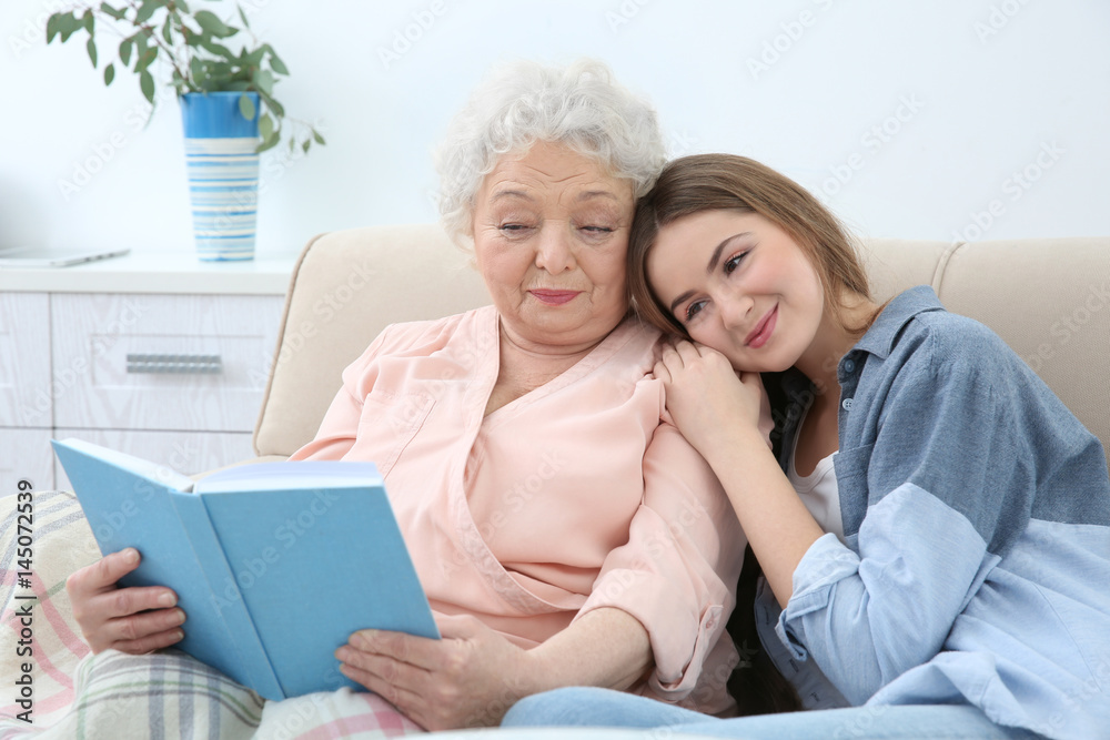 Beautiful girl with grandmother reading book on couch at home Beautiful girl with grandmother reading book on couch at home
