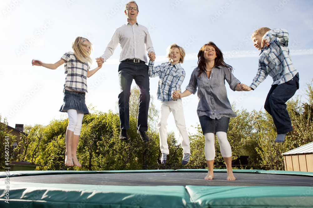 Happy family jumping on trampoline while holding hands in back yard against  sky during sunny day Stock Photo | Adobe Stock