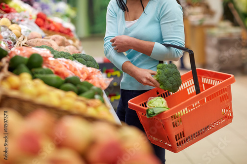 woman with basket buying broccoli at grocery store