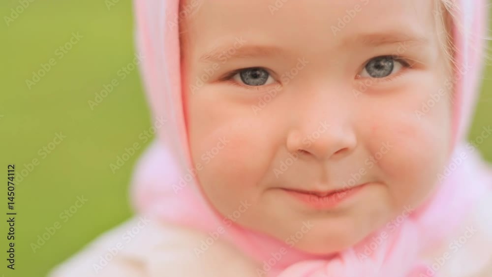 Little Russian girl posing in front of the camera. Smiling and looking close up. On the head is a pink headscarf. Little Russian girl posing in front of the camera. Smiling and looking close up. On the head is a pink headscarf.