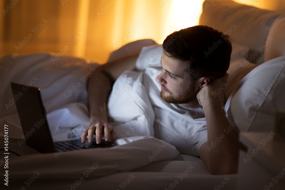 young man with laptop in bed at home bedroom