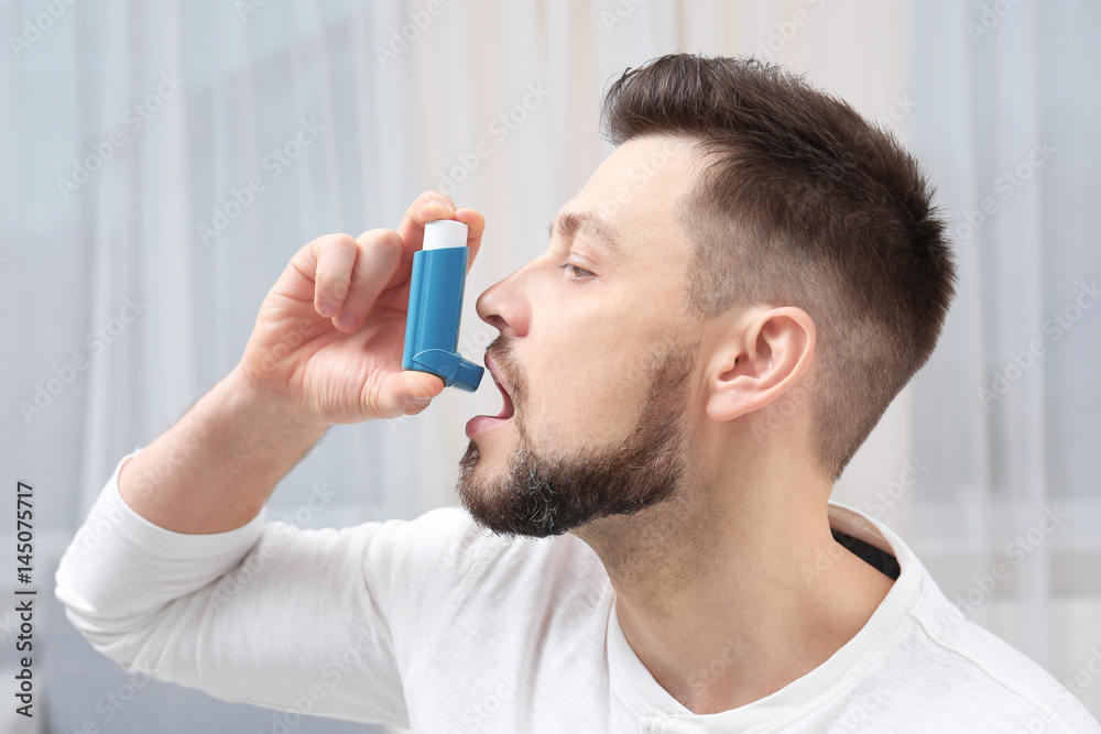 Young man using asthma inhaler at home Young man using asthma inhaler at home