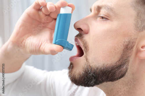 Fototapeta Naklejka Na Ścianę i Meble -  Young man using asthma inhaler, closeup