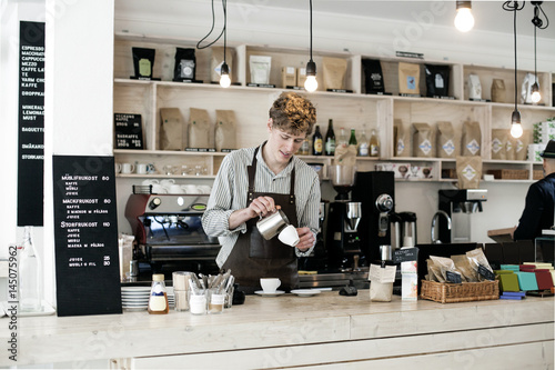 Young barista preparing cappuccino at counter in coffee shop