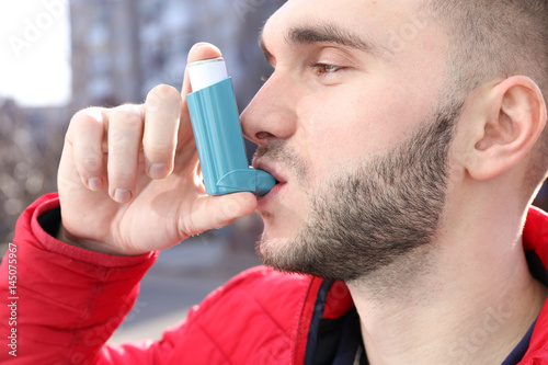 Fototapeta Naklejka Na Ścianę i Meble -  Young man using asthma inhaler on street