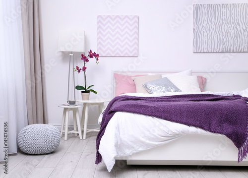 Comfortable bed with soft lilac coverlet and pillows in light modern room photo