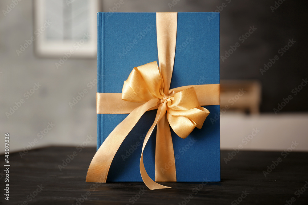 Naklejka premium Book with ribbon as gift on wooden table