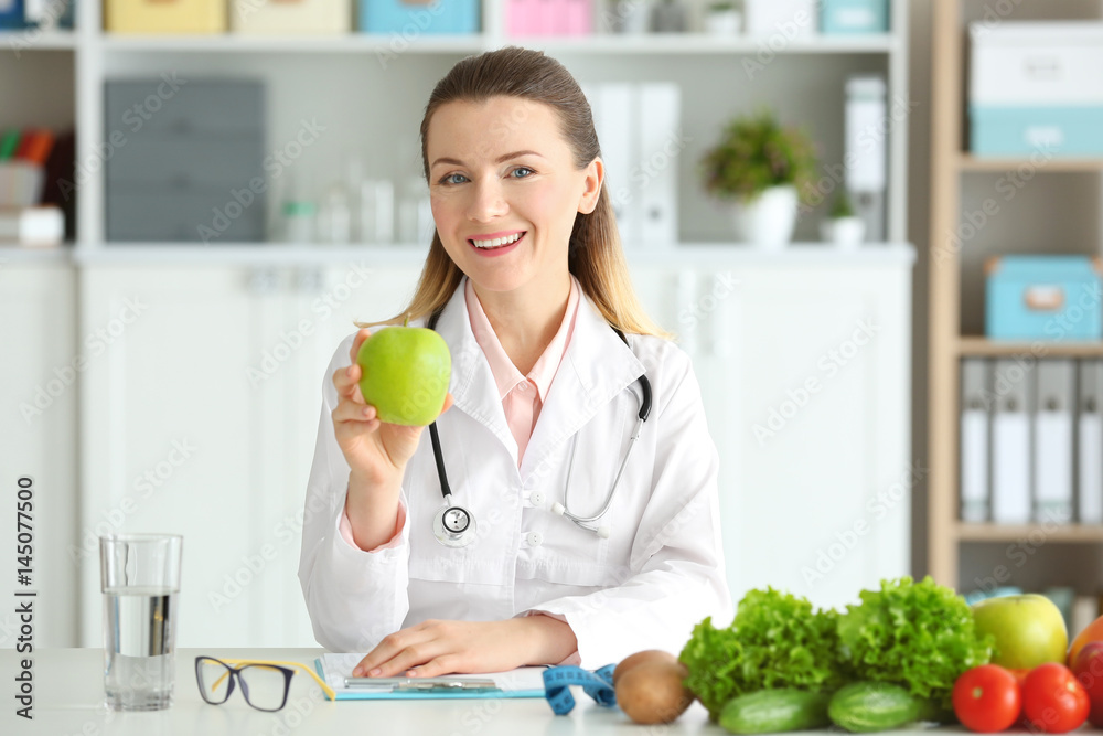 Young female nutritionist with apple in her office