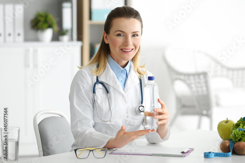 Young female nutritionist with bottle of water in her office