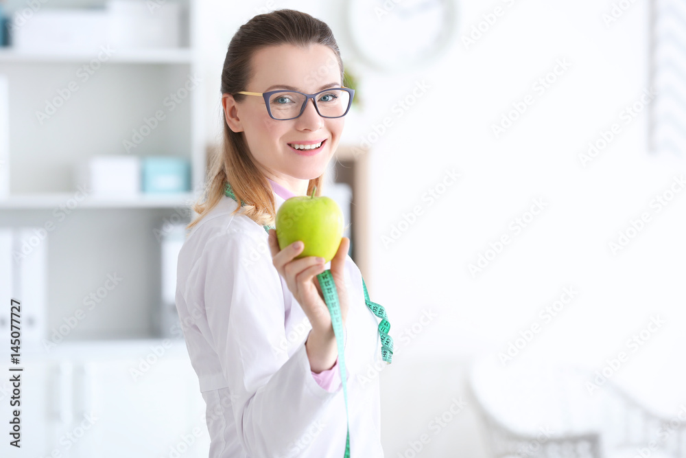 Young female nutritionist standing with apple in her office Young female nutritionist standing with apple in her office