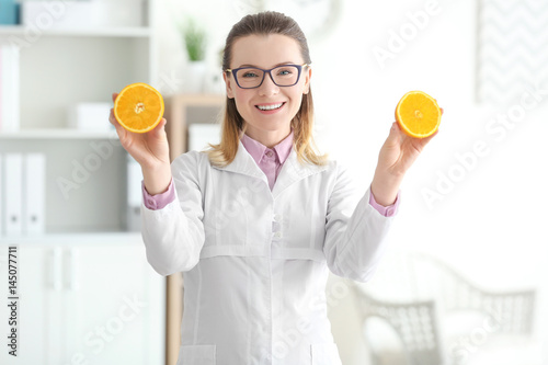 Young female nutritionist standing with orange in her office