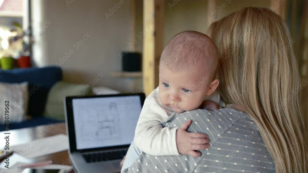 Unrecognizable mother with son in the arms, working on laptop Unrecognizable mother with son in the arms, working on laptop