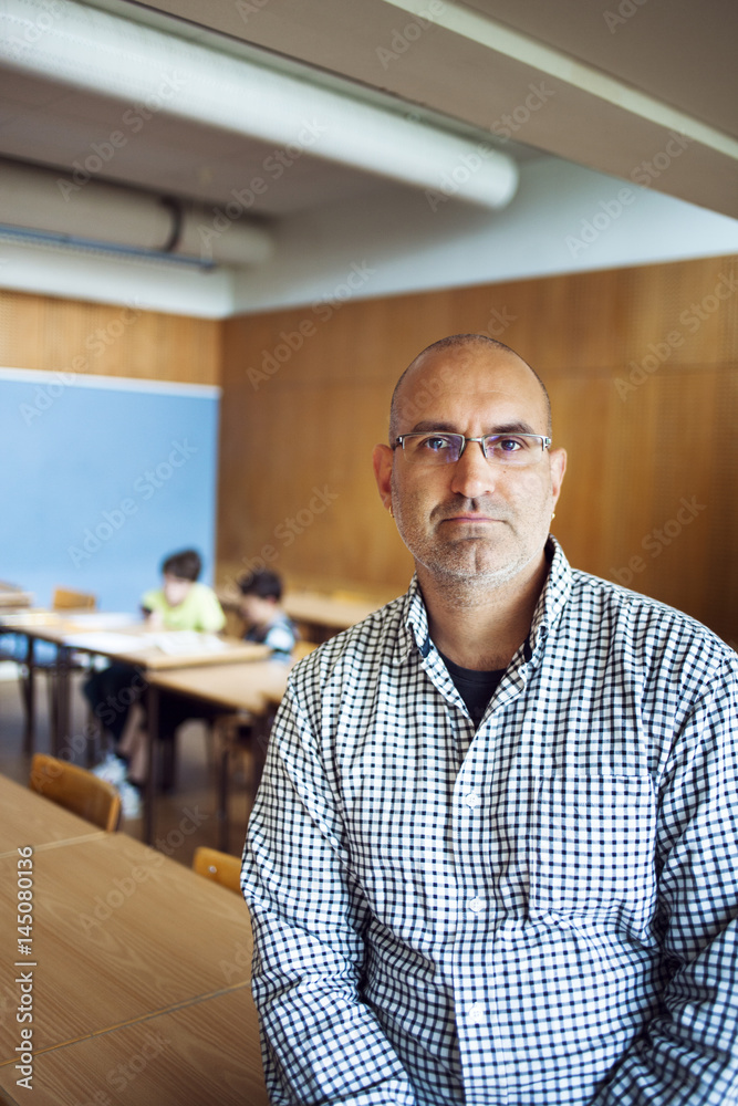 Portrait of confident teacher sitting on desk in classroom Portrait of confident teacher sitting on desk in classroom