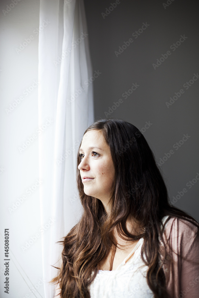 Thoughtful woman looking through window at home Thoughtful woman looking through window at home