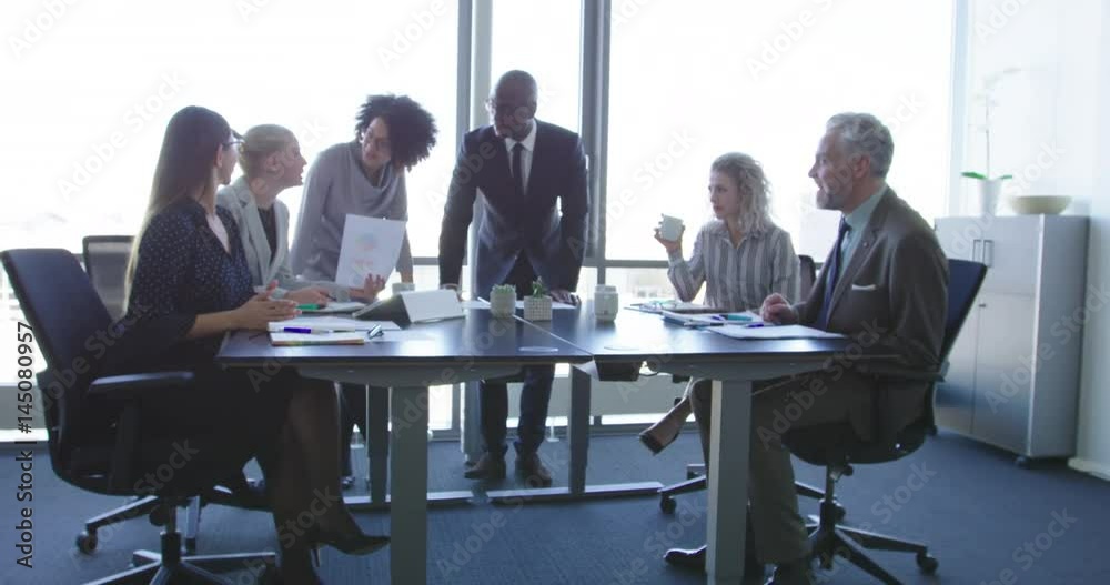 Group of diverse business people in formal clothing inside their office discussing or looking at information on a laptop computer