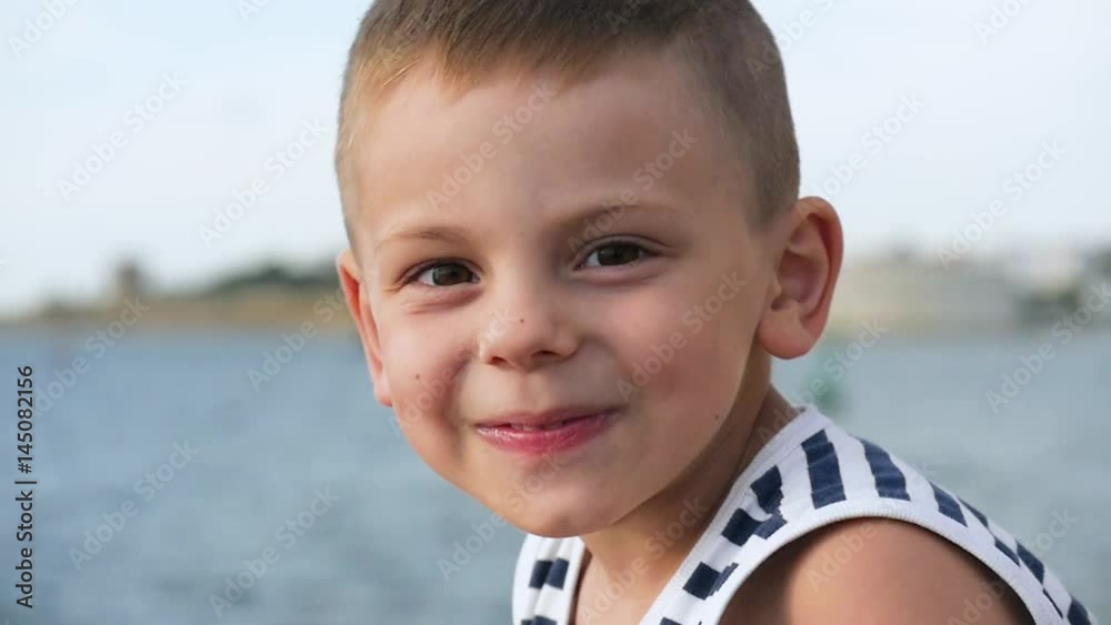little boy in a striped shirt playing with binoculars in front of the sea and the coast