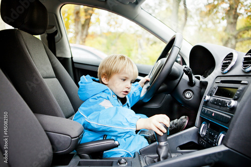 Cute boy sitting on driver's seat in car photo