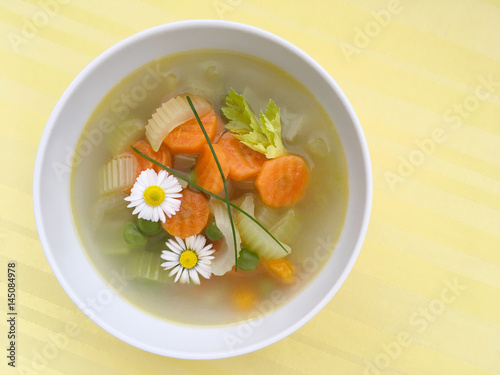 Vegetable spring soup with carrot, peas and celery. Decorated by edible daisy flowers. Top view.