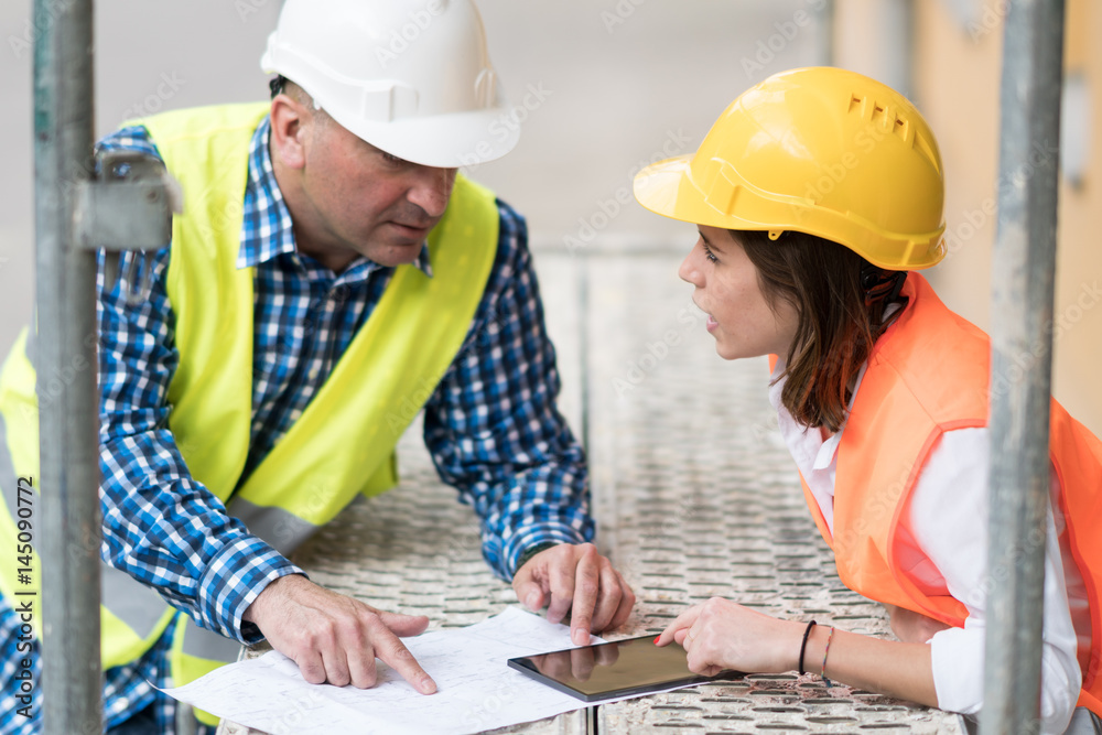 Two construction engineers holding plans and inspecting the construction site Two construction engineers holding plans and inspecting the construction site