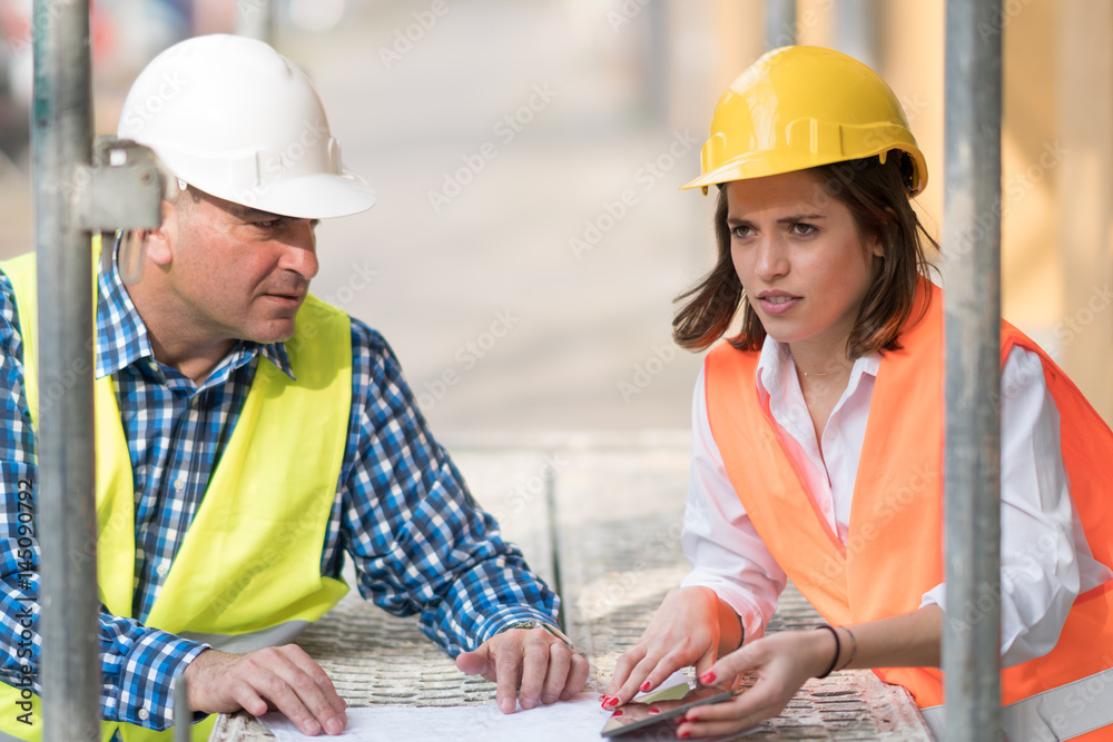 Two construction engineers holding plans and inspecting the construction site Two construction engineers holding plans and inspecting the construction site