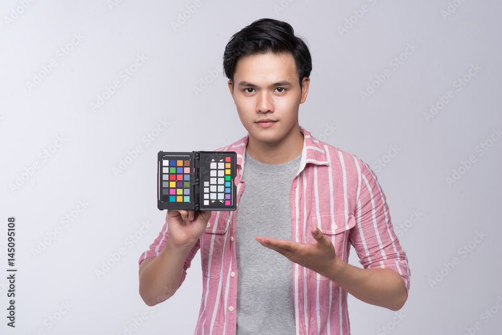 Young asian photographer holding color checker card, while working in studio Young asian photographer holding color checker card, while working in studio