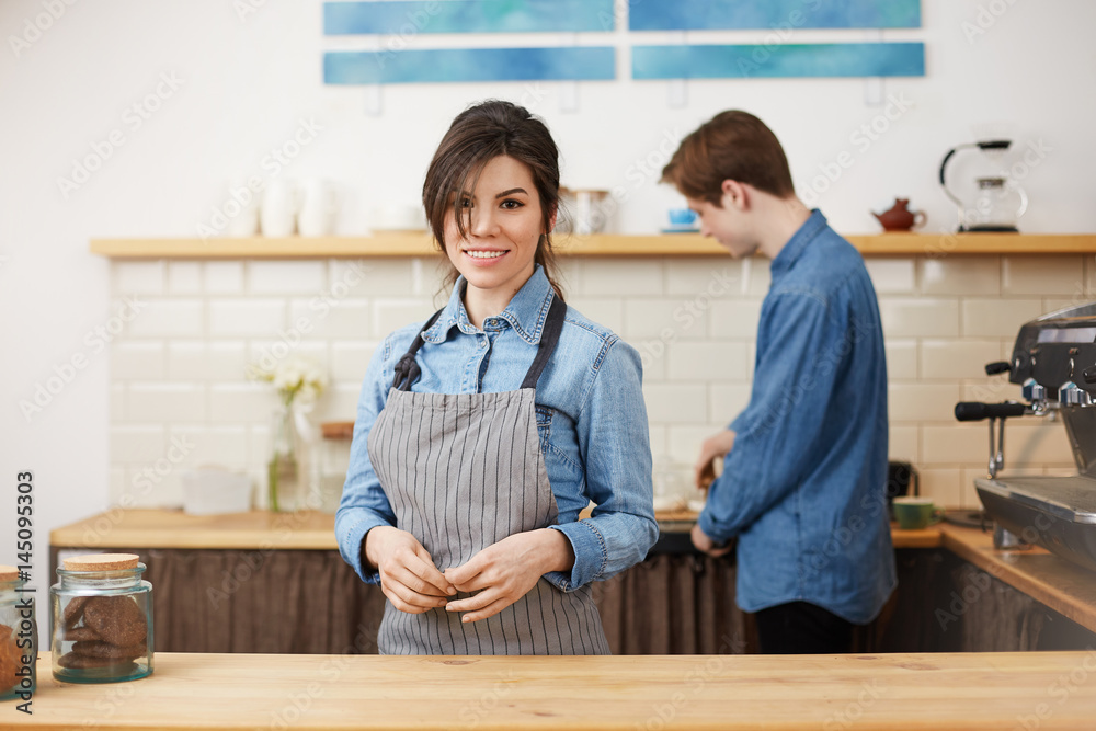 Fototapeta premium Beautiful female barista in uniform smiling cheerfully taking orders.