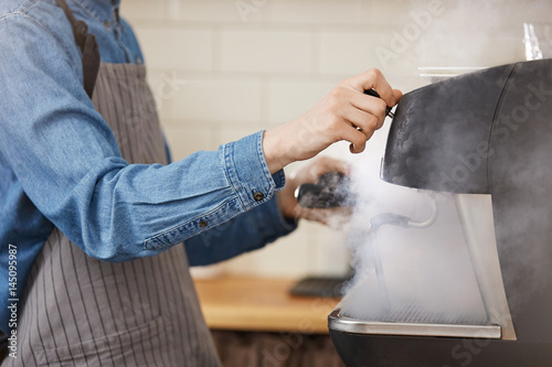 Male barista in uniform washing brewing gadgets using steamer. © Cookie Studio