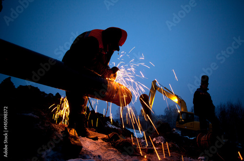 A worker grinds a pipe on the construction of a pipeline
