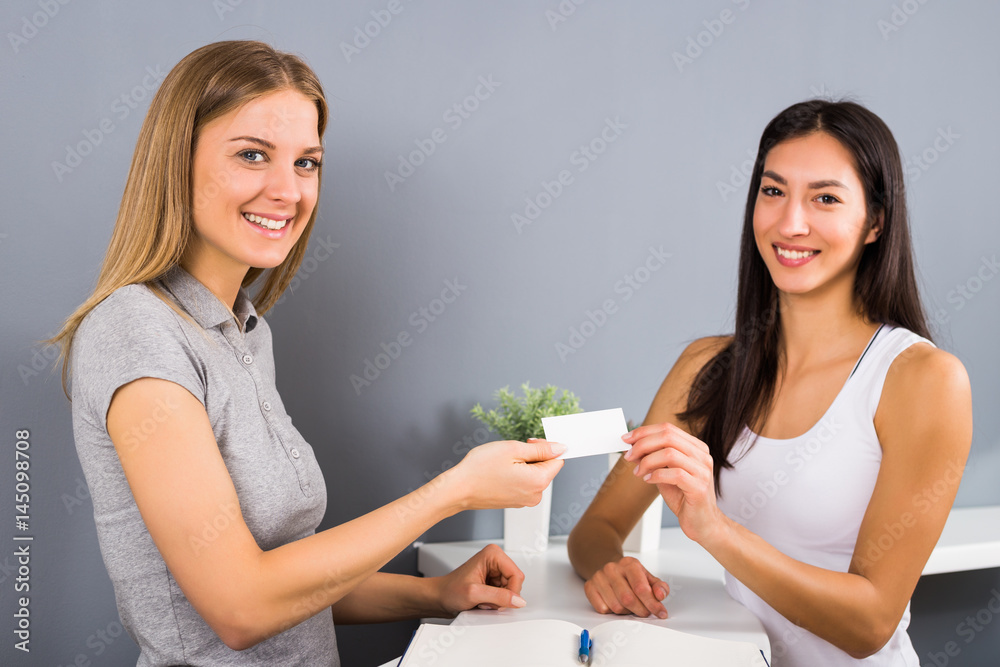 Woman receptionist of the fitness center is giving a membership card to sporty woman who came to exercise. Woman receptionist of the fitness center is giving a membership card to sporty woman who came to exercise.