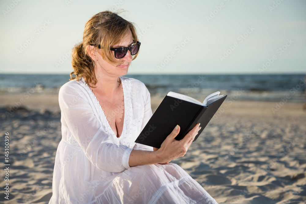 Woman sitting and reading book on beach Woman sitting and reading book on beach