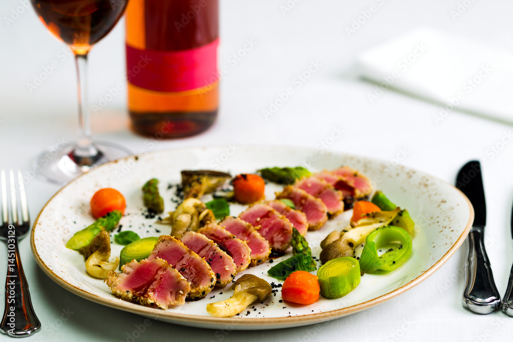Salad of tuna and vegetables with a glass of wine and a bottle of wine on a white tablecloth, studio light