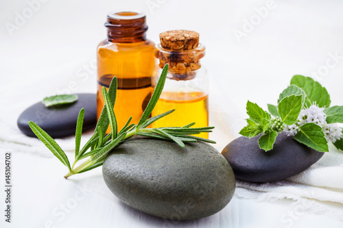 Alternative health care and herbal medicine . Close Up fresh rosemary and peppermint leaves on spa stone with essential oil bottle setup on white wooden table. Selective focus shallow depth of field.