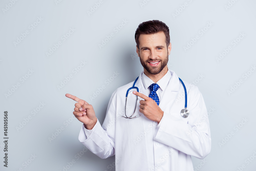 Glad dentist with beaming smile standing against white background and pointing on copy-space Glad dentist with beaming smile standing against white background and pointing on copy-space
