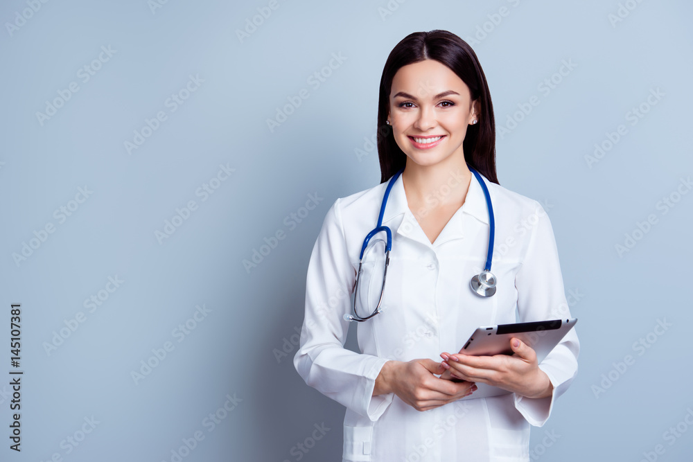 Smiling cheerful nurse in uniform portrayed on gray background holding digital tablet Smiling cheerful nurse in uniform portrayed on gray background holding digital tablet