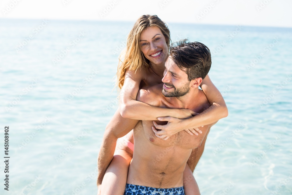 Man piggybacking girlfriend on shore at beach