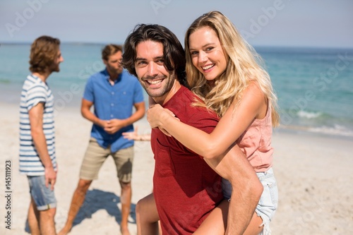 Boyfriend piggybacking girlfriend by friends at beach
