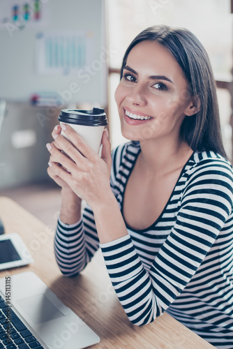 Vertical close up photo of beautiful happy manager drinking coffee while having a rest at work