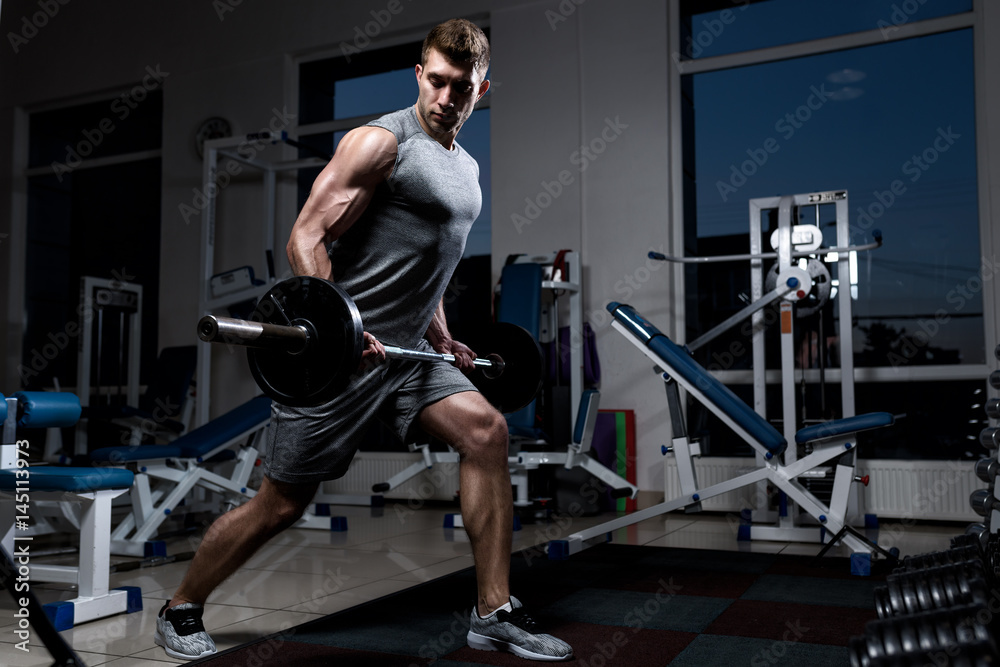 Young muscular man in a vest with a barbell training in the gym Young muscular man in a vest with a barbell training in the gym