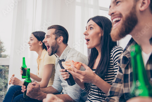 Canvas Print Close up of four friends, fans of games, sitting at the sofa in nice cozy home, watching the game and showing excitement, amazement, shock