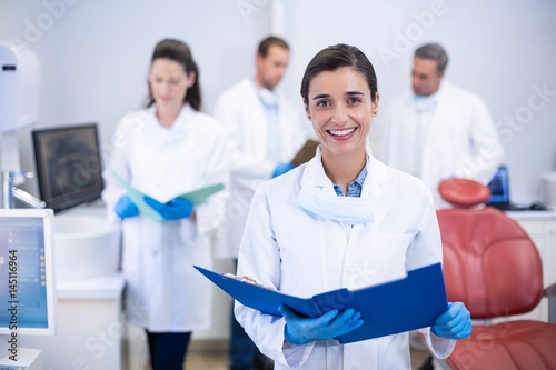 Smiling dentist holding file at dental clinic