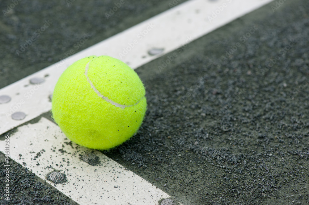 Yellow tennis ball on the corner line of a clay tennis court with a shallow depth of field and copy space