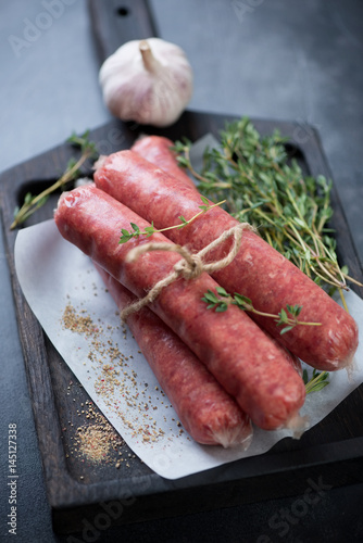 Close-up of raw marbled beef sausages with fresh thyme, garlic and spices, selective focus