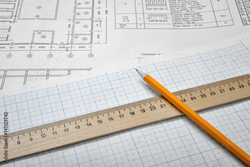 Open blueprints on wooden table background with a pencil and a ruler lying beside.