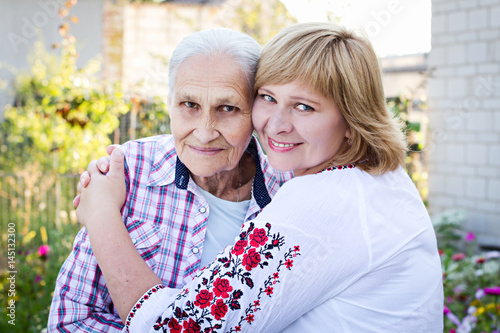 Middle-aged woman hugging her mother in nature. Real emotions of happiness. Mothers Day. Senior Woman With Adult Daughter In Park photo