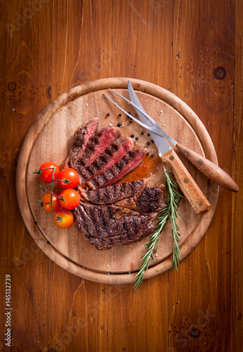 Obraz na płótnie Sliced medium rare grilled Beef steak Ribeye with cherry tomatoes on cutting board, selective focus w salonie