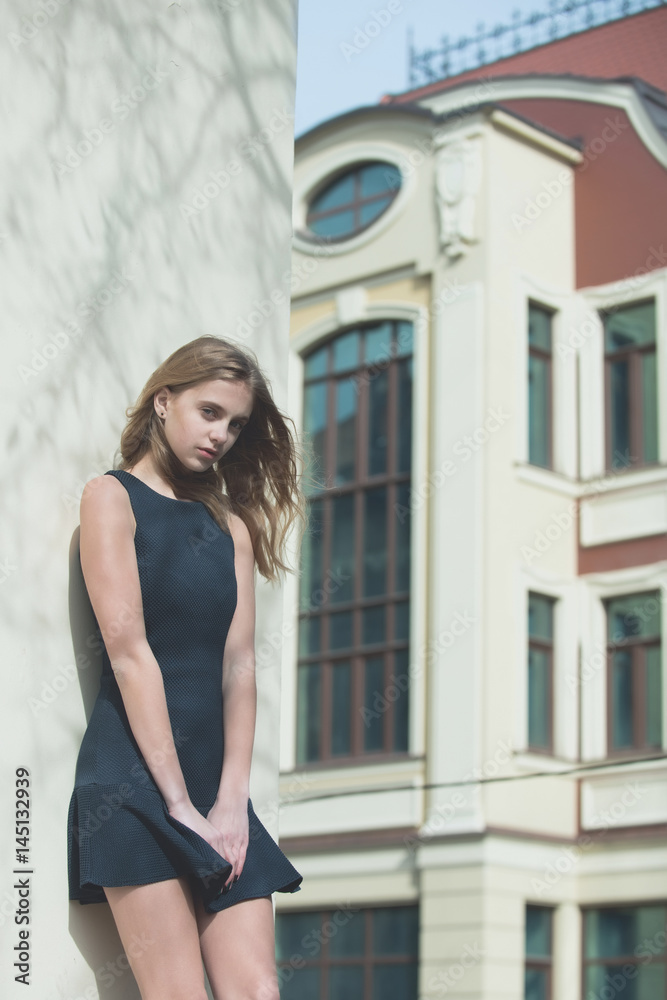 Fototapeta premium Pretty girl in fashionable black dress at building wall